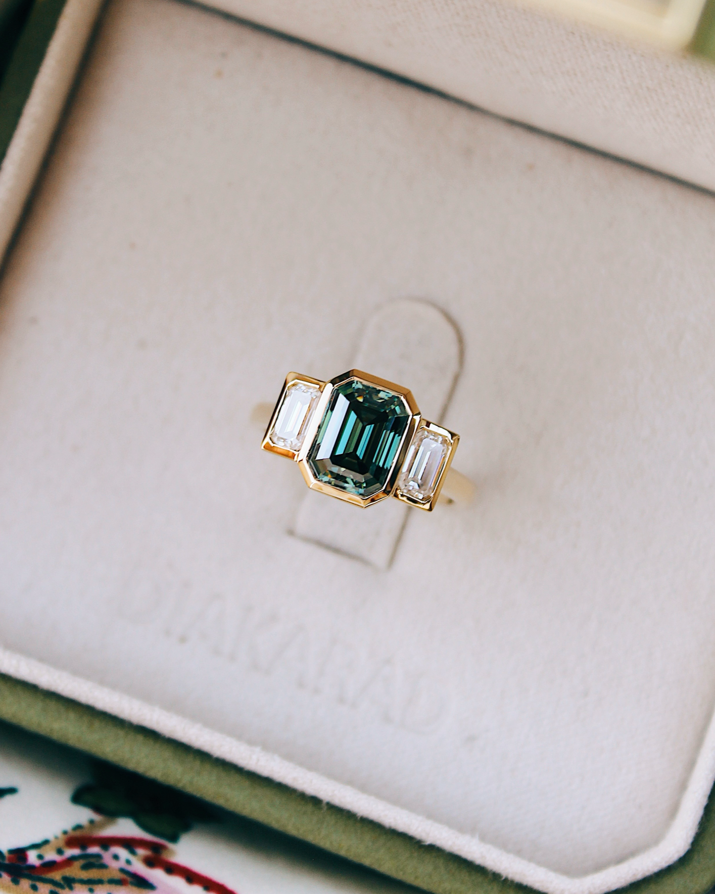 18K Trilogie Goldring Olivia mit einem grünen Emerald Cut Moissaniten und zwei Baguette Seitensteinen, Draufsicht