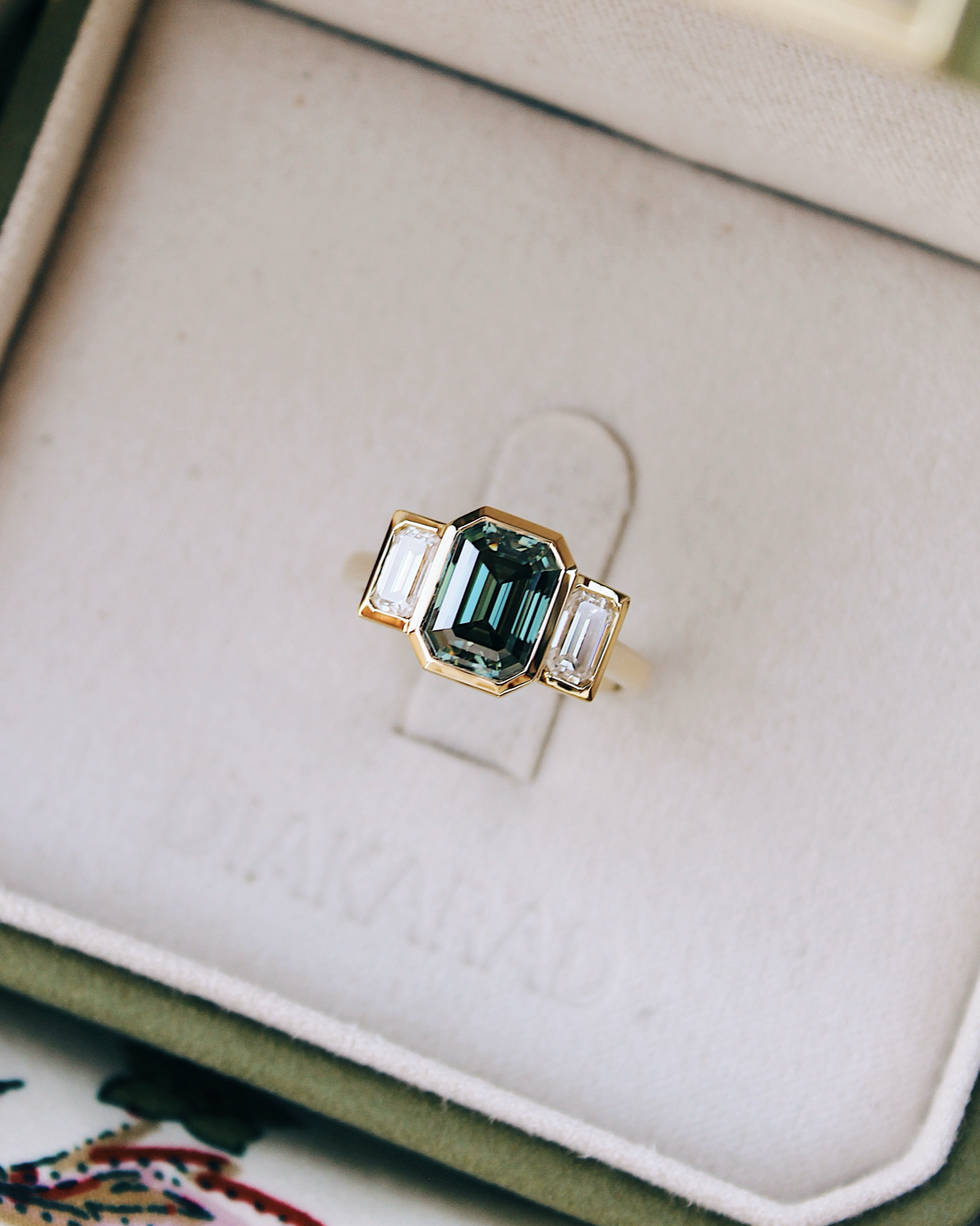 18K Trilogie Goldring Olivia mit einem grünen Emerald Cut Moissaniten und zwei Baguette Seitensteinen, Draufsicht