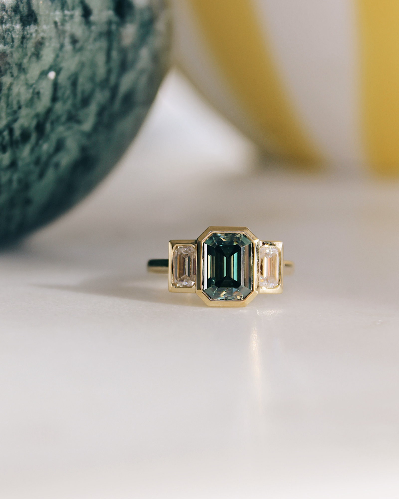 18K Trilogie Goldring Olivia mit einem grünen Emerald Cut Moissaniten und zwei Baguette Seitensteinen.