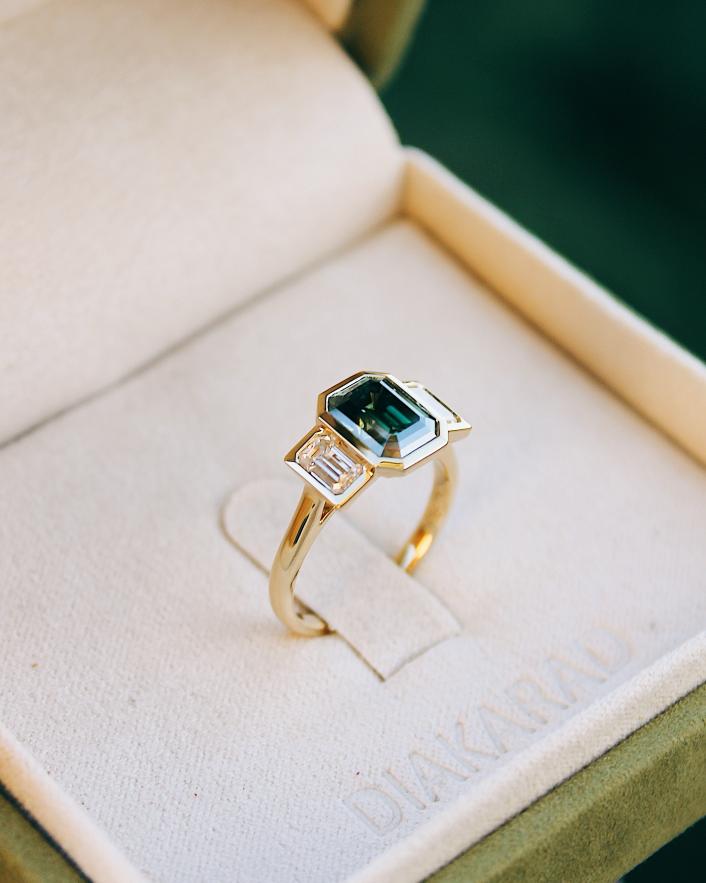 18K Trilogie Goldring Olivia mit einem grünen Emerald Cut Moissaniten und zwei Baguette Seitensteinen, in der Ringschachtel