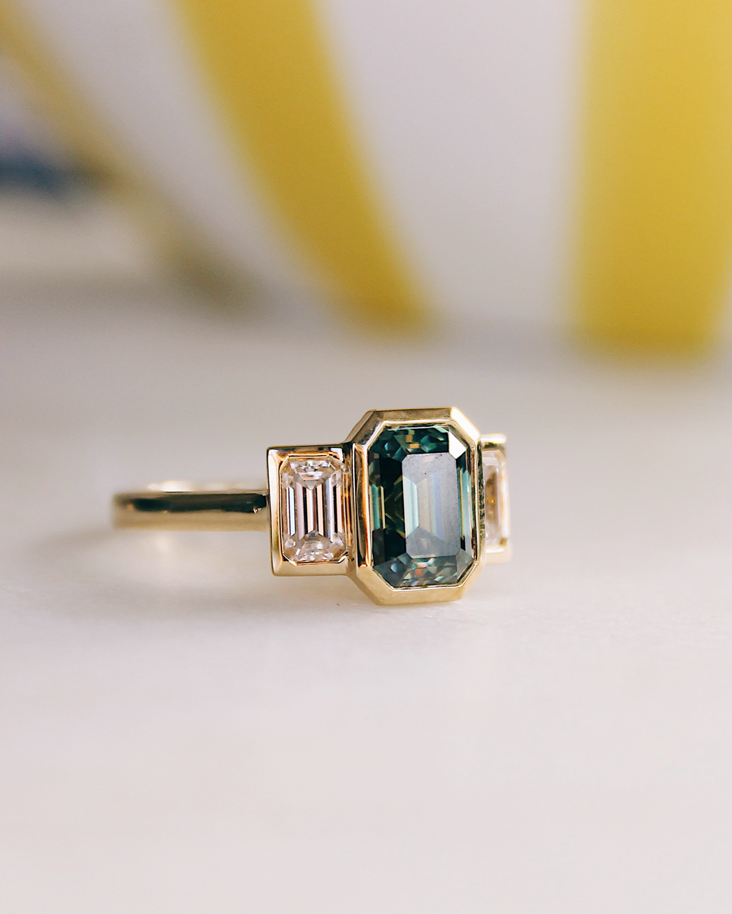 18K Trilogie Goldring Olivia mit einem grünen Emerald Cut Moissaniten und zwei Baguette Seitensteinen, Seitenansicht