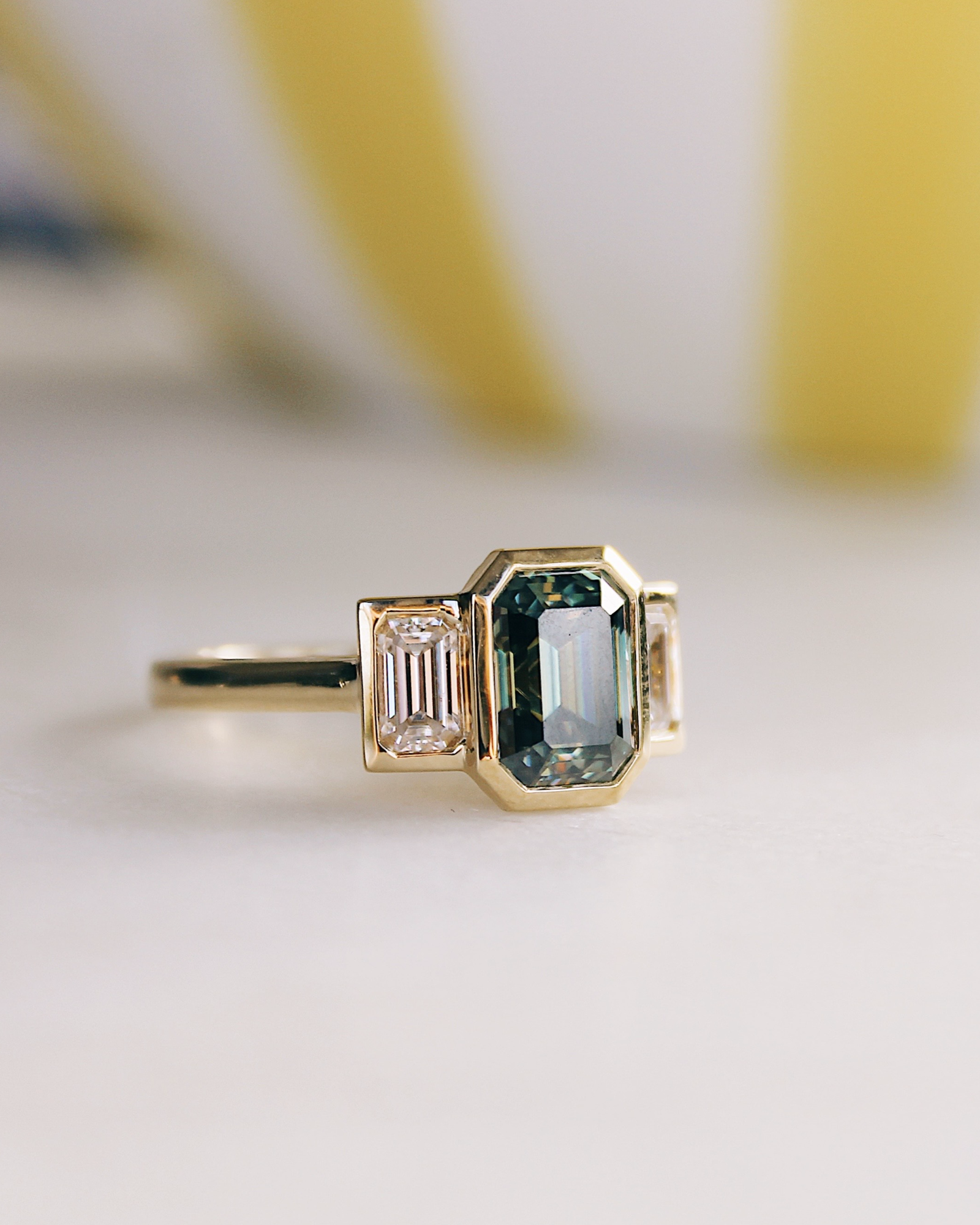 18K Trilogie Goldring Olivia mit einem grünen Emerald Cut Moissaniten und zwei Baguette Seitensteinen, Seitenansicht